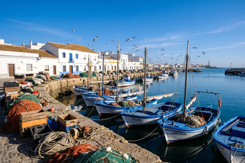 Barcas de pesca azules y blancas amarradas en un puerto atlántico, con redes y cajas apiladas en el muelle